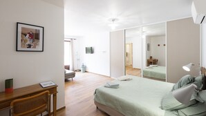 Une chambre à coucher avec un lit, un bureau, une chaise, un miroir et un tableau encadré au mur.