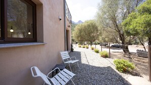 L’extérieur d’un bâtiment, avec une fenêtre, une porte et un chemin de gravier menant à un espace extérieur aménagé pour s’asseoir.