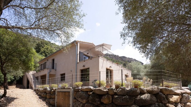 Un bâtiment à deux étages, doté d’une entrée avec un mur en pierre, d’un balcon et offrant une vue sur un paysage montagneux.