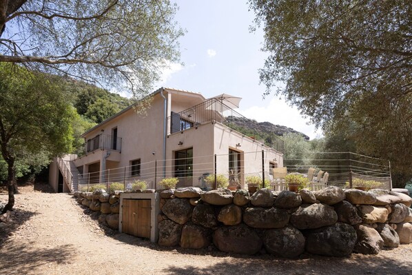 Un bâtiment à deux étages, doté d’une entrée avec un mur en pierre, d’un balcon et offrant une vue sur un paysage montagneux.