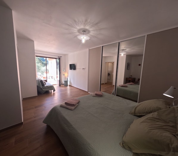 Ein Schlafzimmer mit Bett, Spiegel, Fernseher und Blick ins Freie.