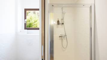Une salle de bain avec une douche, des toilettes et une fenêtre donnant sur un espace verdoyant.