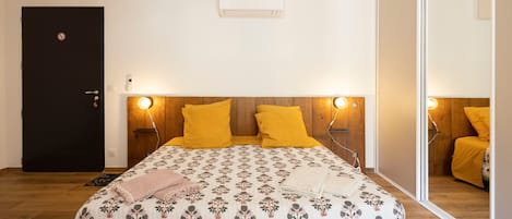 A bedroom with a bed, wooden headboard, bedside lamps, a black door, and a mirror.