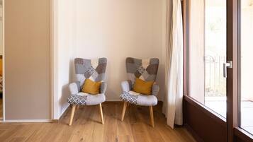 Two armchairs with patterned upholstery and wooden legs, positioned in a corner with a wooden floor and a view through a glass door.