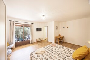 Un dormitorio con cama, escritorio, silla, televisor y balcón con cortinas.