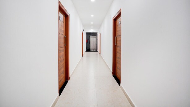 A long, narrow hallway with wooden doors on both sides and a tiled floor. - Suite Indiranagar Jeevan Bhima Nagar (Bengaluru)
