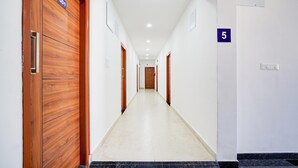 A hotel hallway with wooden doors, numbered signs, and a tiled floor. - Suite Indiranagar Jeevan Bhima Nagar (Bengaluru)