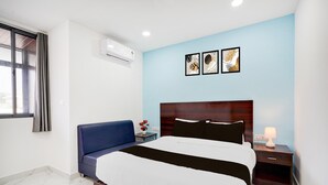 A bedroom with a bed, a nightstand, a lamp, a blue sofa, and artwork on the wall. - Suite Indiranagar Jeevan Bhima Nagar (Bengaluru)