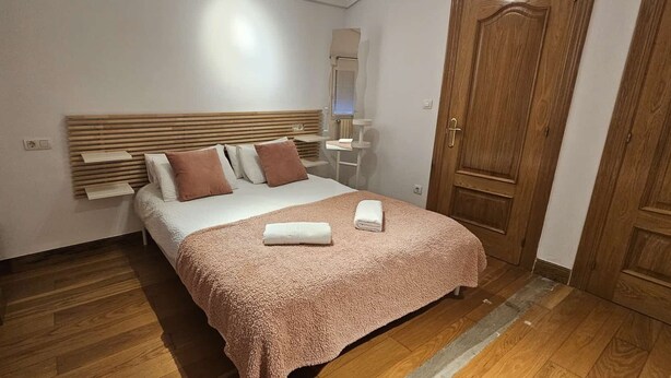 A bedroom with a wooden headboard, a bed with a pink blanket, a bedside table, and a wooden wardrobe.