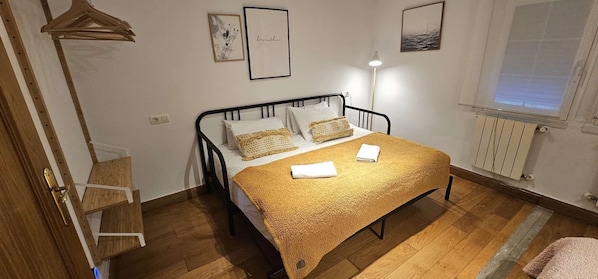 A bedroom with a bed, bedside lamps, a radiator, and a window.