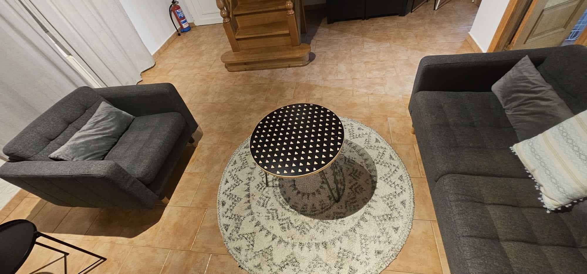 Una sala de estar con una mesa redonda, dos sofás y una alfombra estampada.