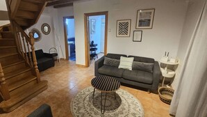 A living room with a staircase, a gray sofa, a patterned coffee table, and a white lamp.