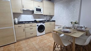 A compact kitchen with a washing machine, a microwave, and a dining area with a table set for two.
