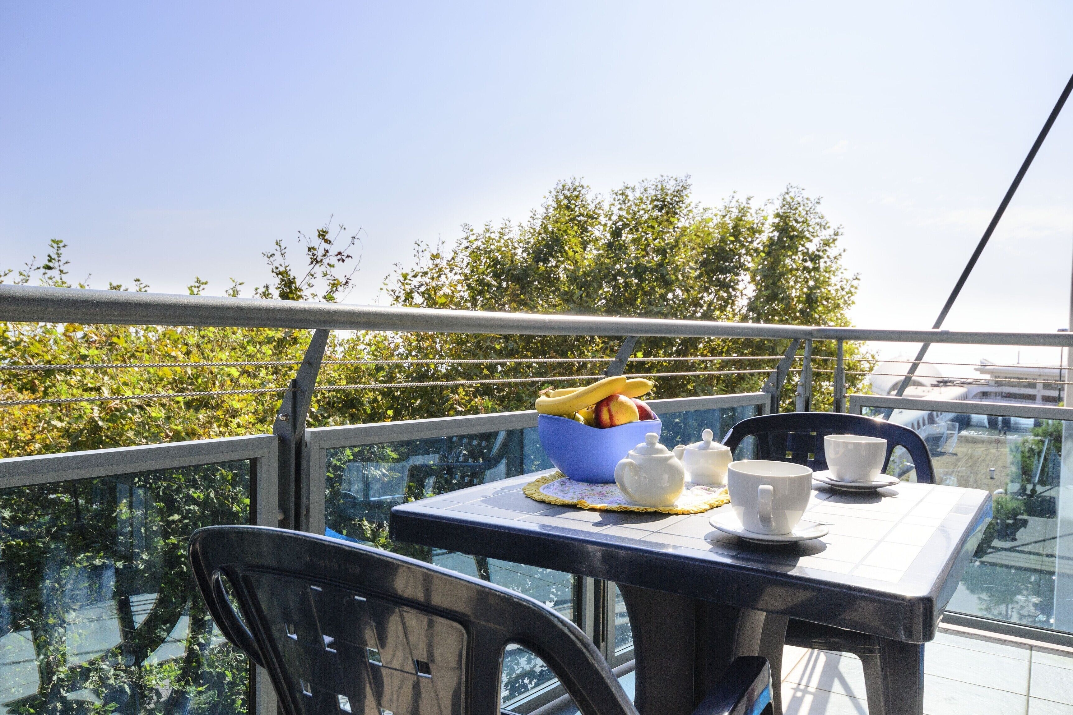Een balkon met een ontbijttafel, inclusief een fruitschaal, theepot, kopjes en schotels.