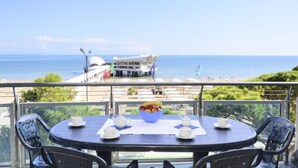 A round table with a bowl of fruit, white cups, and a teapot on a balcony overlooking the sea. - Lignano Sabbiadoro Seafront Stay (Lignano Sabbiadoro)