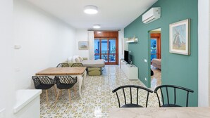 Un espacio habitable compacto con comedor, sofá, televisor y balcón con vistas.