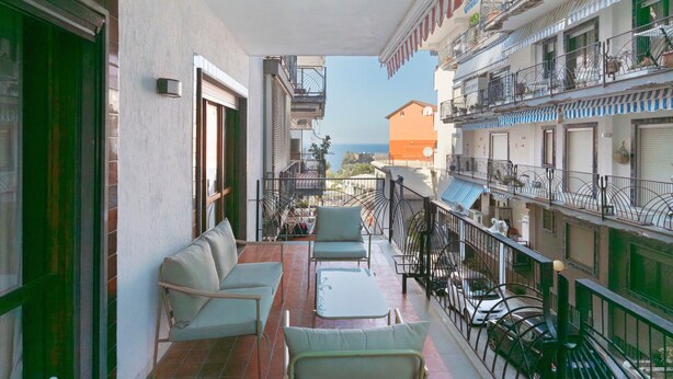 Un balcón con mobiliario exterior, vista al mar y un edificio con balcones.