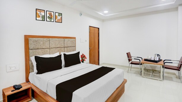 A hotel room with a bed, bedside table, and a small table with chairs. - Deluxe With Twin Bed Vishnu Grand (Hanmakonda)