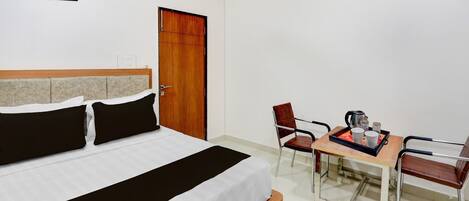 A hotel room with a bed, a wooden door, a table with chairs, and a coffee maker.