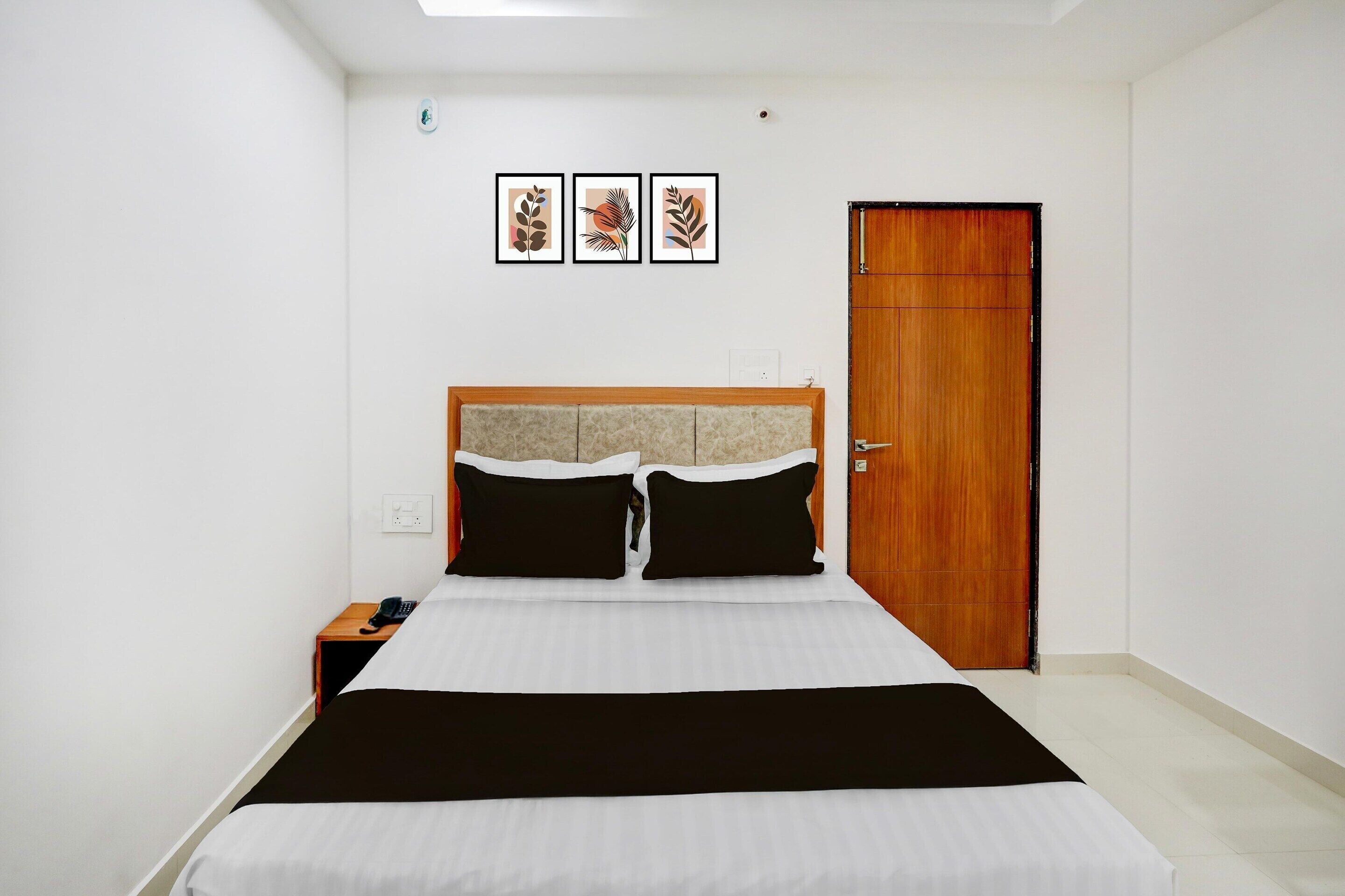 A hotel room with a bed, a wooden door, and three framed pictures on the wall.