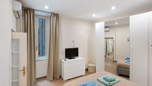 Een slaapkamer met een bed, een televisie op een dressoir, een kledingkast en een raam met gordijnen.