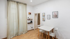 Een kamer met een witte tafel en stoelen, een houten vloer, een deur en een wand met ingelijste foto's.