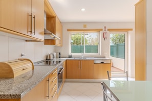 A modern kitchen with wooden cabinets, a granite countertop, a built-in oven, and a window with a view of greenery. - #337 Great 2BR Apartment | Terrace in Albufeira (Albufeira)