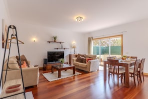 A living room with a sofa, TV, coffee table, dining table with chairs, and a window with curtains. - #337 Great 2BR Apartment | Terrace in Albufeira (Albufeira)