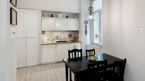Une cuisine de taille modeste, avec des meubles blancs, une table à manger en bois et une fenêtre agrémentée de rideaux.