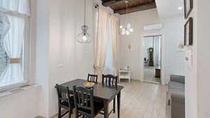 Un coin repas avec une table, des chaises et un lustre. On aperçoit un canapé et une petite table avec une lampe au fond.