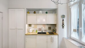 Une cuisine avec des meubles blancs, un plan de travail en bois, un évier et une fenêtre avec des rideaux.