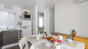 Ett modernt kök med kylskåp, mikrovågsugn och diskho. Det finns ett matbord med frukostmat och en soffa i bakgrunden.