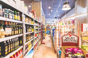A grocery store aisle with shelves stocked with various products, a sign for 'SALATI PREZIOSI', and a checkout area in the background. - Jesolo Family Resort (Jesolo)