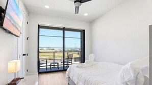A bedroom with a bed, a TV, a desk, a chair, and a balcony with a view. - Stay in Pure Luxury with Resort-Style Amenities! (New Braunfels)