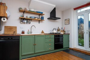 Una cocina con gabinetes verdes, lavavajillas, estufa y ventana con vistas al exterior.
