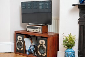 Ein Fernsehgerät auf einem Holzboden mit zwei Lautsprechern, einem gerahmten Bild und einer Vase mit Blumen.