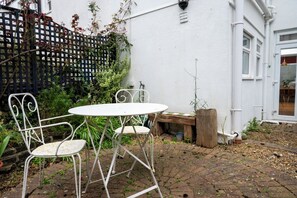 A patio with a white metal table and chairs, surrounded by plants and a wooden post. - Modern 2BDR Retreat | Near Beach & City Centre (Brighton and Hove)