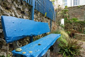 Un banco azul con un muro de piedra y vegetación al fondo.