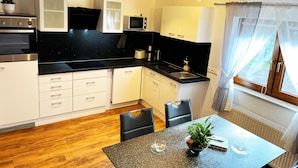 A modern kitchen with white cabinets, a black countertop, and a dining area with a table and chairs. - Viktorias Villa (Schleiden)