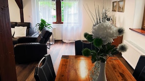 A living room with a wooden dining table, black leather sofa, and a potted plant. - Viktorias Villa (Schleiden)