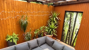 A wooden deck with a gray cushioned seating area, potted plants, and string lights. - Viktorias Villa (Schleiden)