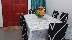 A dining area with a table set for four, a red door, teal curtains, and a mirror on the wall.