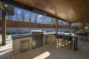 An outdoor kitchen with a grill, bar stools, and a dining table. - Cedar Pointe Texoma Sleeps 18Swimming Pool (Kingston)
