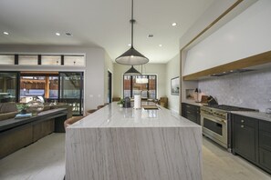 Uma cozinha espaçosa com uma ilha de mármore grande, armários escuros e uma luminária pendente moderna.