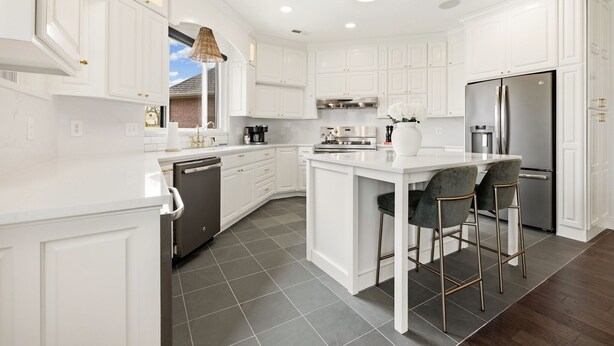 Una cocina moderna con armarios blancos, una isla central con taburetes de bar, un refrigerador de acero inoxidable y un lavavajillas.
