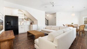 Cocina moderna con armarios blancos, un refrigerador negro y un comedor con mesa blanca y sillas de mimbre.
