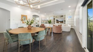 Una sala de estar moderna con una mesa de comedor redonda de madera, sillas tapizadas de color verde, un sofá blanco y un sillón rosa.