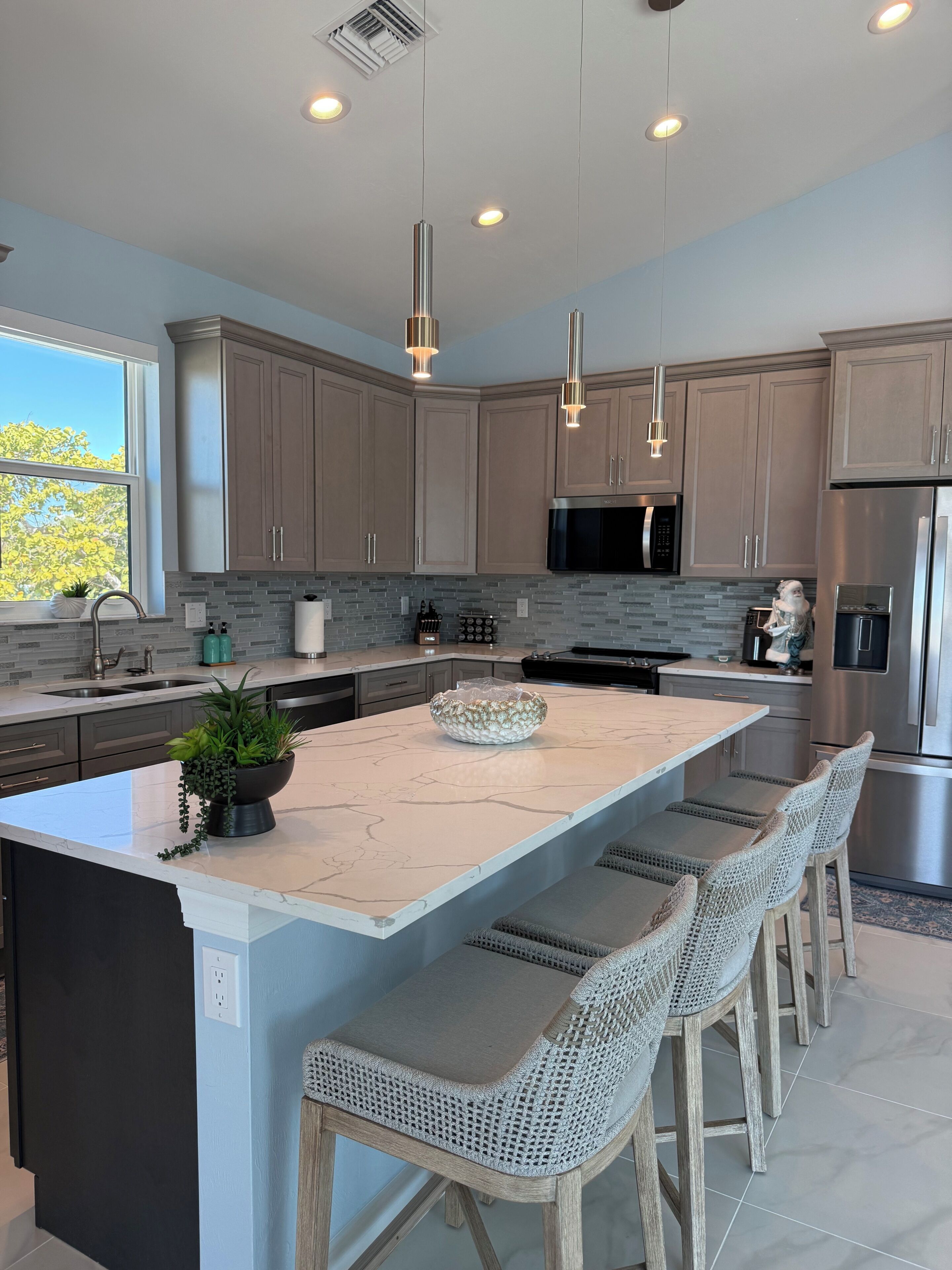 A modern kitchen with a large island, stainless steel appliances, and pendant lighting.