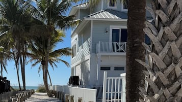 A beach pathway lined with palm trees leading to a white building with balconies.