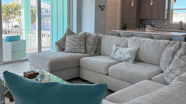 A modern living room with a sectional sofa, a glass coffee table, and a view of the outside. - Ft. Myers Beach across street to Beach Golf Cart (Fort Meyers Beach)